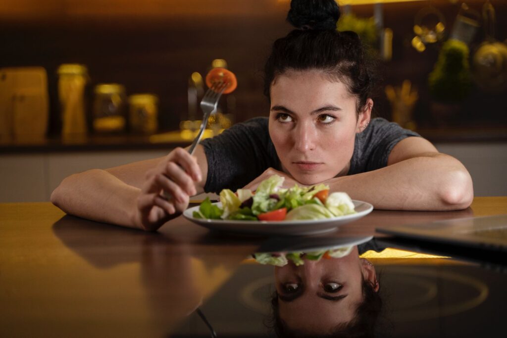Frau an einem Tisch sitzend vor einem Teller voller Salat